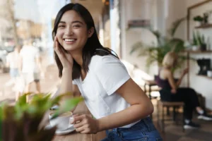 happy asian woman sitting restaurant near window smiling camera
