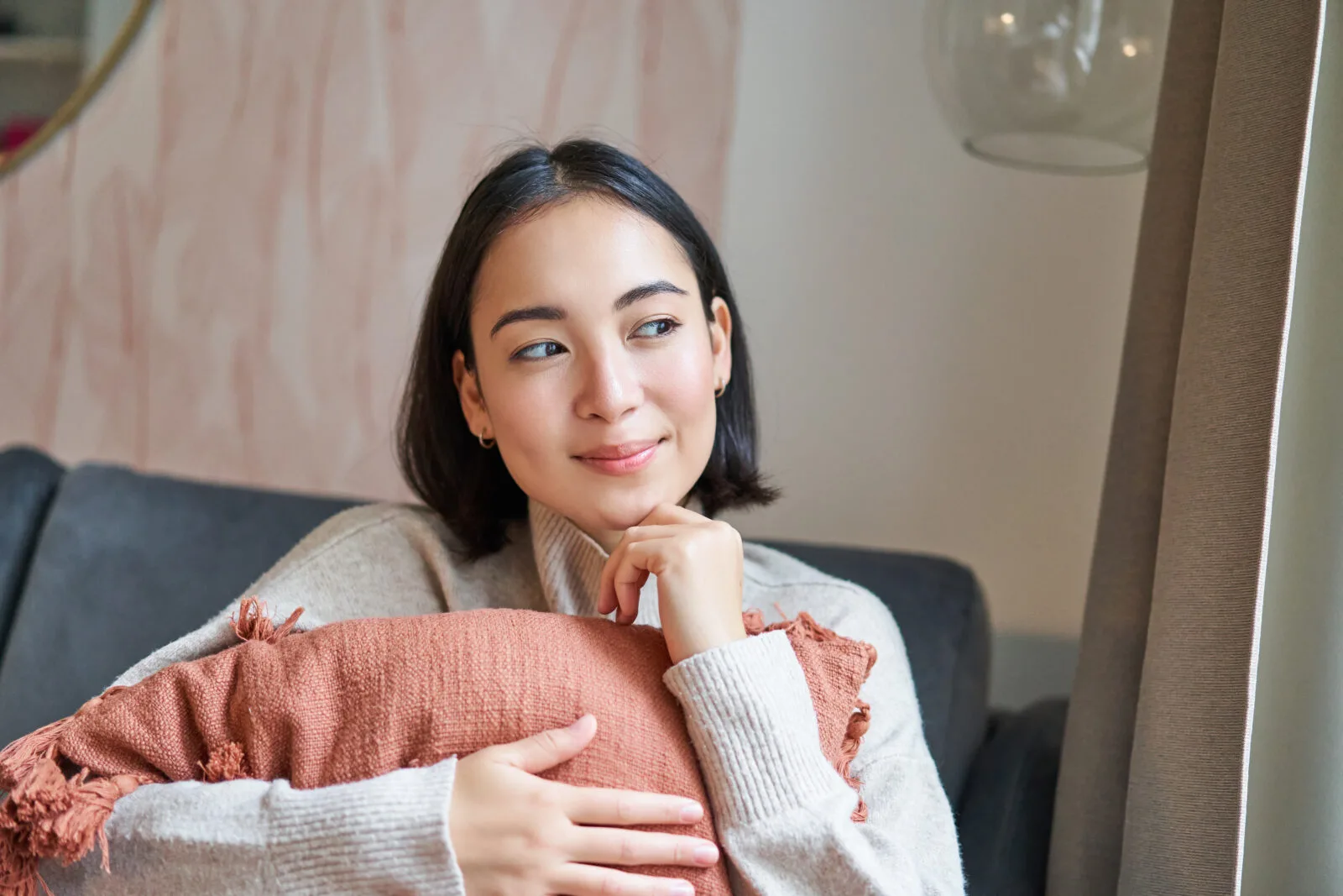 portrait asian woman feeling cozy her home hugging pillow sofa looking thoughtful smili