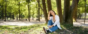 young people beautiful asian girl sits near tree park rests smiling looking into distance