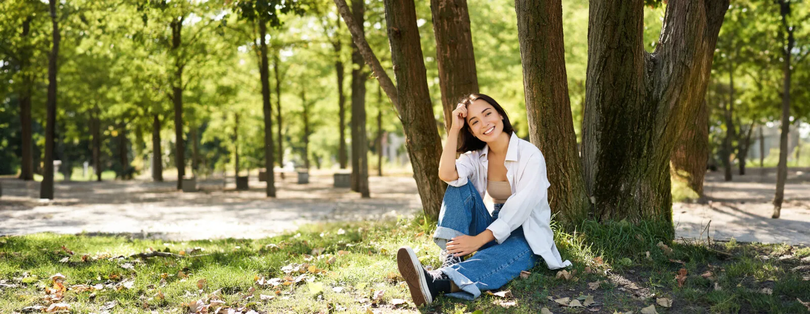 young people beautiful asian girl sits near tree park rests smiling looking into distance